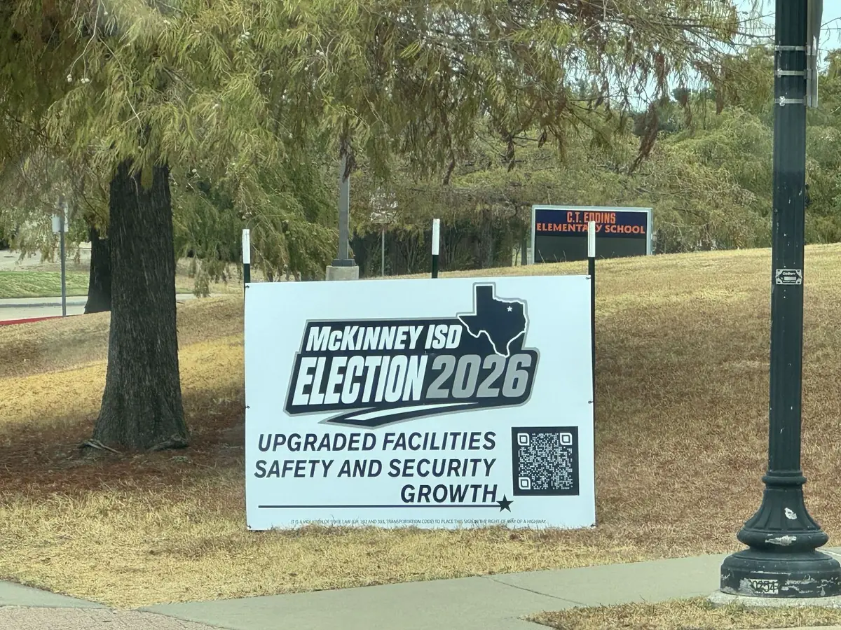 A white McKinney ISD Election 2026 sign on a grassy slope under trees, with the C.T. Eddins Elementary School sign visible behind it.